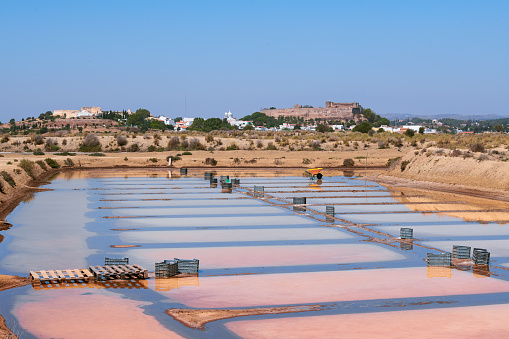 Traditional, flooded Salt flats, with Castro Marim village in the background.  Photo taken on a windless,  summer sunny day. These salt flats are located in the south of Portugal, by the Guadiana River, near the Spanish border. The area is named Sapal de Castro Marim and Vila Real de Santo António Natural Reserve.