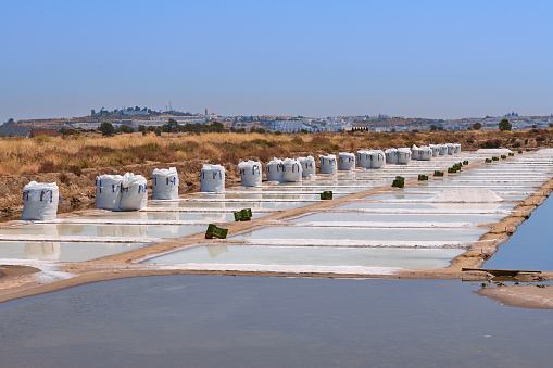 Big bags of sea salt, ready for collection in a traditional salt flat. Photo taken near Castro Marim on a summer sunny day. These salt flats are located in the south of Portugal, by the Guadiana River, near the Spanish border. The area is named Sapal de Castro Marim and Vila Real de Santo António Natural Reserve. The Spanish side of Guadiana can be seen on the background.