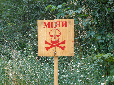 A wooden sign with a skull drawing warning that the area was mined. War concept. TEXT TRANSLATION: MINES
