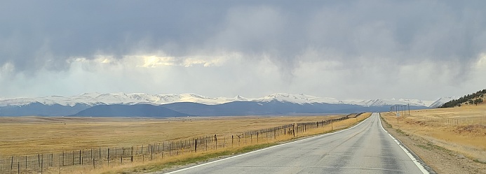 Edge of a snowstorm in view while riding into it on a roadway with open prairie fields on both sides.