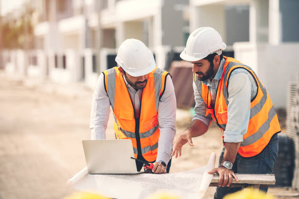 zwei kaukasische bauingenieure und architekten, die auf der baustelle mit laptop und blaupausen auf dem tisch zusammenarbeiten. immobilien-baustellenprojekt. - bauingenieur stock-fotos und bilder