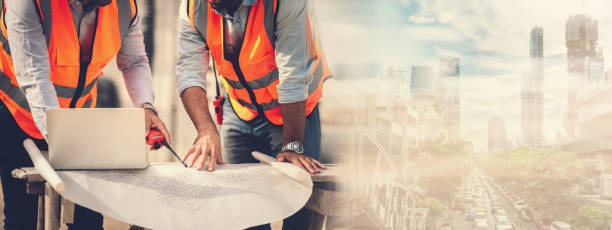 istock Panoramic banner two caucasian man construction engineers and architects working together on new city project at construction site using laptop and blueprints. Real estate mega project work site. 1414051147