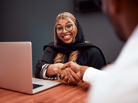 Interview handshake between muslim HR manager and employee, greeting, welcome and thank you hand gesture at hiring meeting. Female hijab Human Resources worker congratulating man on new job promotion