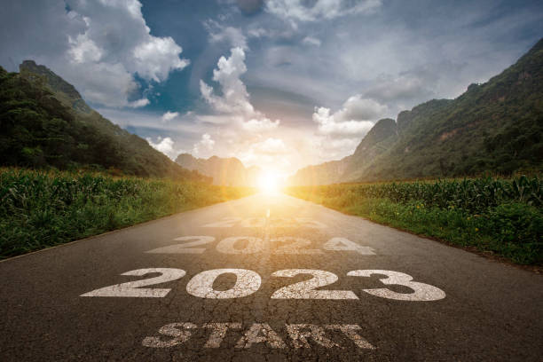 2023, el año nuevo 2023 o el comienzo del concepto de la palabra 2023 se escribe en la carretera en medio de la carretera de asfalto con un telón de fondo de montaña al atardecer, conceptos de planificación y desafíos. - finish line fotografías e imágenes de stock