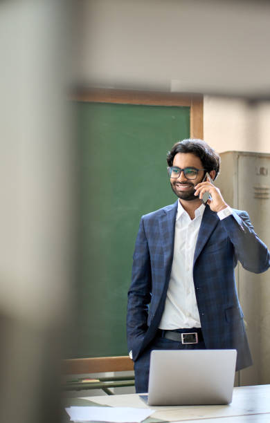 smiling young indian business man wearing suit talking on phone at workplace. - color image bus discussion expertise imagens e fotografias de stock