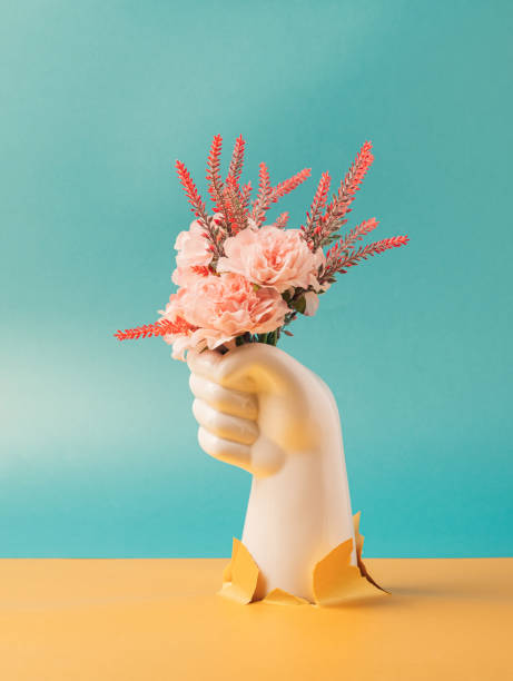 istock White plastic hand holding pink flowers on a two tone background. 1414064417