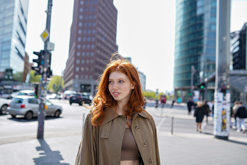 Teen stylish redhead girl standing on big city urban street skyscrapers background looking away and dreaming of future, thinking of new opportunities while walking in downtown outdoor.