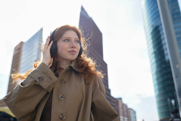 adolescente ruiva usando fones de ouvido ouvindo música na cidade grande. - new life audio - fotografias e filmes do acervo