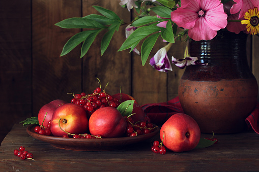 Authentic dark still life with nectarines, red currants and a bouquet in a clay jug.
