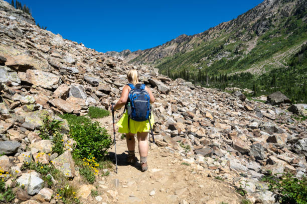 Woman hiker wearing a backpack and using trekking poles makes her way across scree along the Lake Solitude trail in Grand Teton National Park stock photo