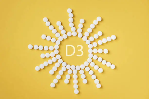 Pills of vitamin D3 in a shape of sun on yellow background top view. Concept of vitamin d3.