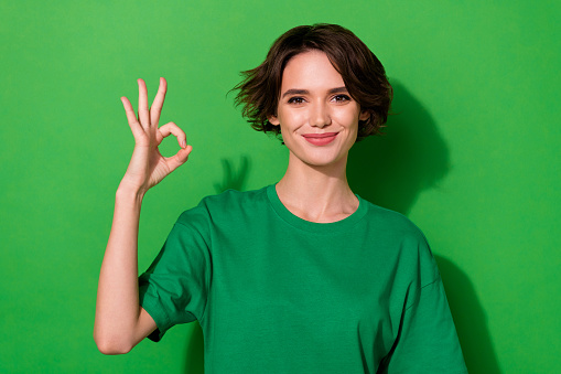 Foto de una mujer bonita y dulce con una camiseta casual que muestra un letrero de okey sonriendo con un fondo de color verde aislado photo