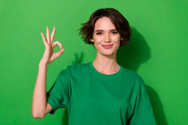 Photo of Photo of pretty sweet woman wear casual t-shirt showing okey sign smiling isolated green color background