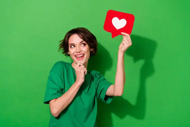 Photo of Photo of charming dreamy woman wear casual t-shirt arm chin looking heart like sign empty space isolated green color background