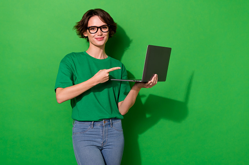 Photo of cute sweet woman wear casual t-shirt arm spectacles pointing modern device isolated green color background.