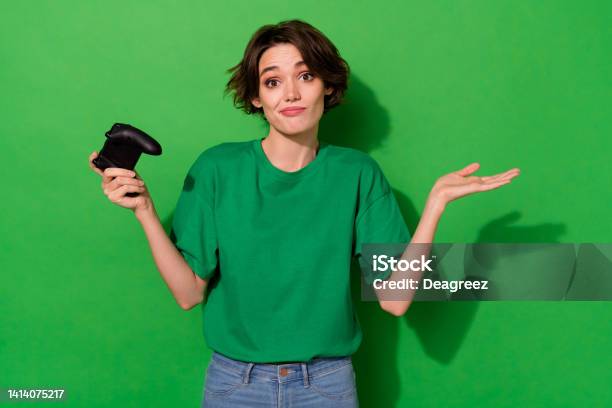 Photo Of Uncertain Funny Woman Dressed Summer Tshirt Holding Playstation Shrugging Shoulders Isolated Green Color Background Stock Photo - Download Image Now