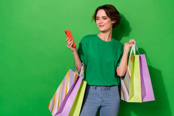 Photo of cute pretty lady wear spring outfit holding shoppers typing device empty space isolated green color background.