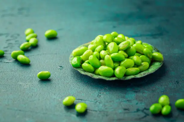 Bowl of raw edamame beans on cyan background
