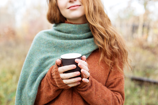 Woman in a light brown sweater. Coffee in a plastic glass. The concept of a lifestyle, autumn, art, cosmetics and care. Nature. The concept of a lifestyle, autumn, art, cosmetics and care.