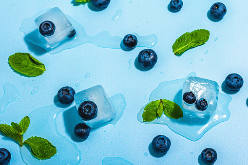 Blueberry, mint, and ice cubes. A trendy hard light, dark shadow, fresh summer blue background, flat lay, top view
