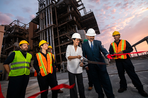 An older caucasian man and a young Asian woman wearing suits visiting a power plant for a ribbon cutting ceremony.