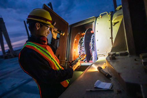 Portrait of a power plant operator wearing coveralls, had hat, high vis vest, and safety glasses working on a turbine at night.
