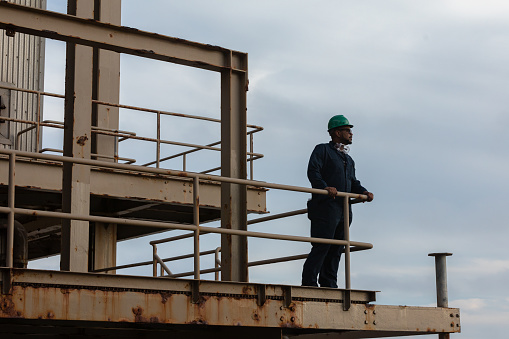 African-American man wearing coveralls and green hard hat standing on on a rusty external walkway at a gas fired power plant on the California coast. 

Authorization was obtained from the FAA for this operation in restricted airspace.