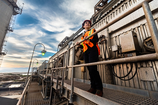 An industrial worker wearing a high vis vest standing on a rusty external walkway at a natural gas power plant on the California coast looking out at the sunset. 

Authorization was obtained from the FAA for this operation in restricted airspace.