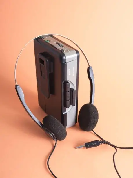 A vintage 1980s S and FM radio player on peach background. These players were ubiquitous throughout the 80s for playing ones favorite music. Shown with period colored background and old school headphones.