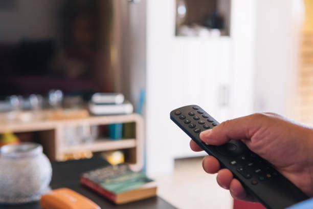 istock Unrecognizable person using the remote control to turn on the TV. Man's hand pressing the buttons of his remote control. Concept of technology 1414086000