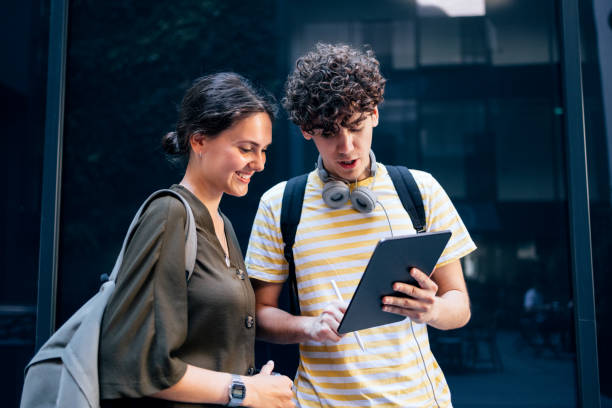 portrait of a couple of students standing and using the digital tablet - digital tablet women enjoyment happiness imagens e fotografias de stock