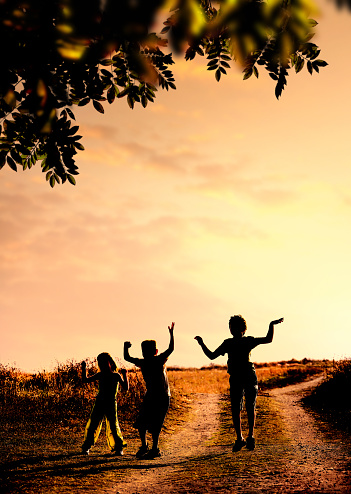 Three children silhouetted by sunset jumping on field.