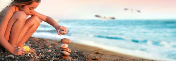 Little girl playing with stones on summer beach vacation over dusk sky