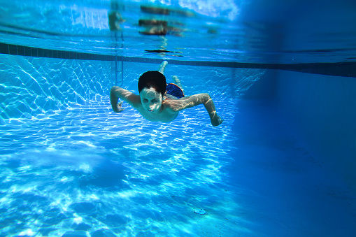 Close up teenage boy swimming underwater in swimming pool in Florida