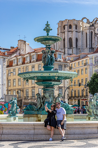 May, 2022. Lisbon, Portugal. A young woman and a man taking a selfie at the square of Dom Pedro IV.