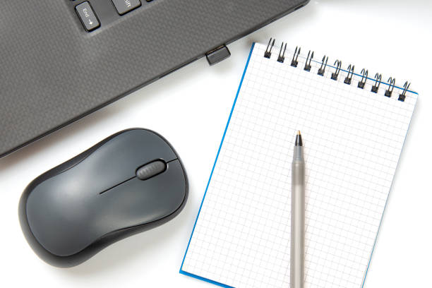 istock Computer wireless mouse, pen and notepad next to a laptop on a white table close-up. Items for office work 1414098168