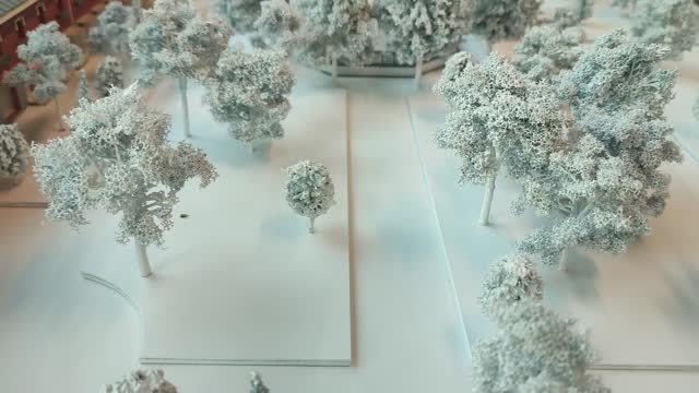 miniature mockup model with snow covered winter trees on white foamboard platforms on the ground and a building in the background - little landscape toy representation