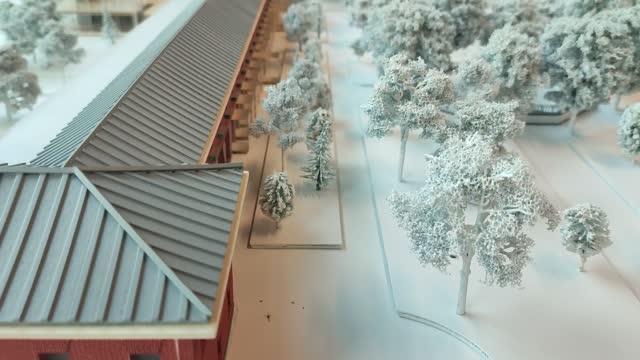 landscape miniature model with white trees in winter covered with snow, next to a large brick building representing Awschwitz barracks