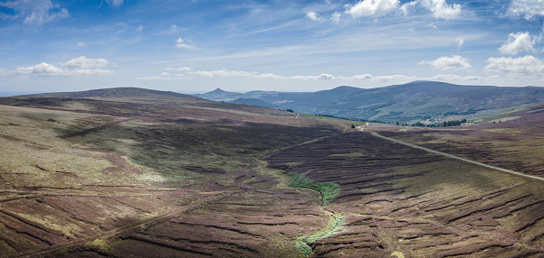 Panoramic aerial view of the Dublin and Wicklow mountains with Sugarloaf mountain in distance, on a bright summer day, with Old Military Road on right of image, looking towards Glencree, and wispy clouds in the sky