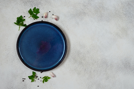 culinary background for the design with copy space for text, empty ceramic plate top view and spices, garlic and green parsley, handmade dish flat lay and mock up
