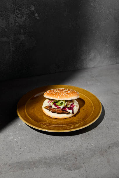 American burger with beef, camambert cheese and jam on plate on gray concrete table. Beef burger with hard shadow and dark stone background. Homemade burger in dark style. Fastfood menu. Junk food.