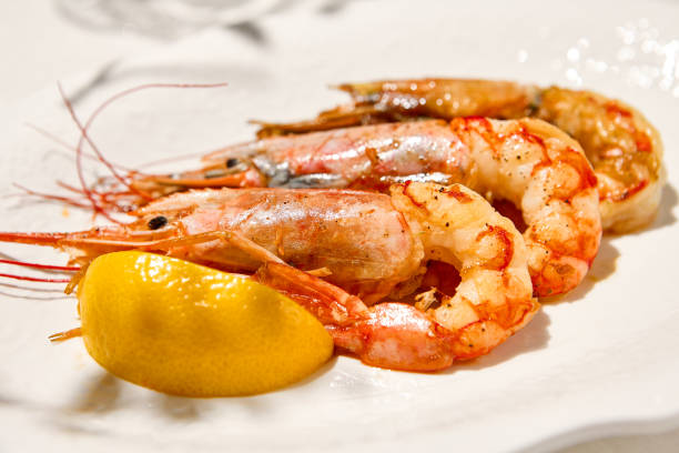 istock Grilled shrimps on light background with shadows. Grilled prawns with lemon on white table. Aesthetic composition with bbq shrimps. Bbq prawns. Grilled seafood. Summer menu. 1414120797
