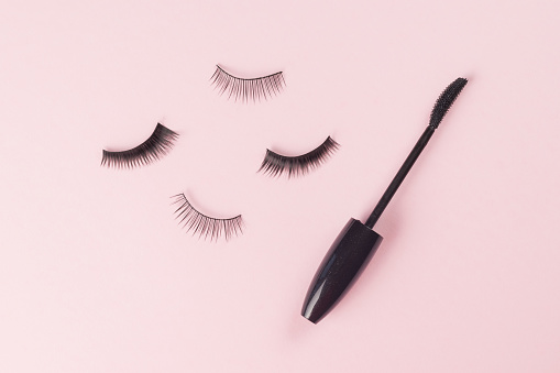 Scattered false eyelashes and a brush on a light pink background. Minimal beauty concept.