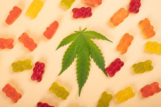 cannabis jelly candies, marijuana multicolored sweets drugs and green leaf on yellow background stock photo