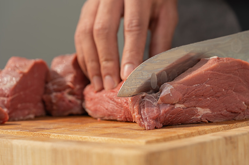 Close up view of a man man slicing meat into pieces using a knife on a wooden board