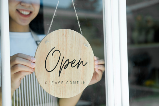 Open business owner woman wearing protection turning
open sign board on glass door in modern cafe coffee shop, cafe restaurant, retail store, small business owner, food and drink concept