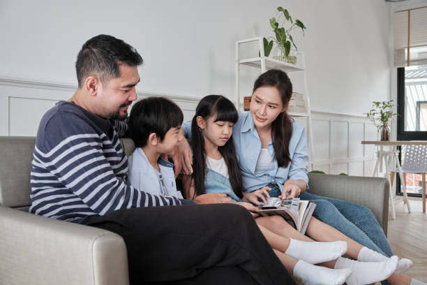 Asian family happiness reading a book together on the sofa in white living room. stock photo