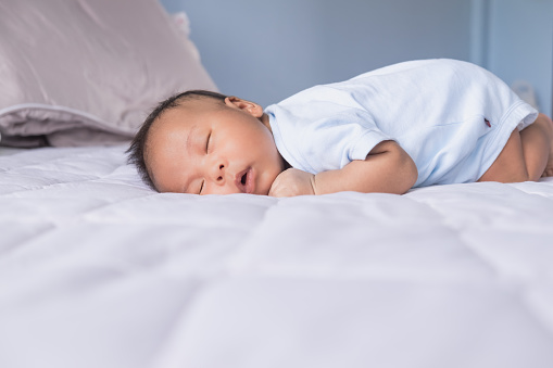 Cute Asian newborn baby boy lying fast sleeping on the bed in the room. Child resting in the bedroom at the home. Breastfeeding or early childhood development concept.