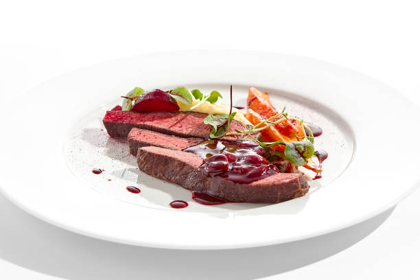 istock Venison steak with baked vegetables isolated on white plate. Meat steak medium rare roasted with carrot, beetroot and mashed potatoes with cherry sauce. Wild meat in restaurant menu. 1414134408