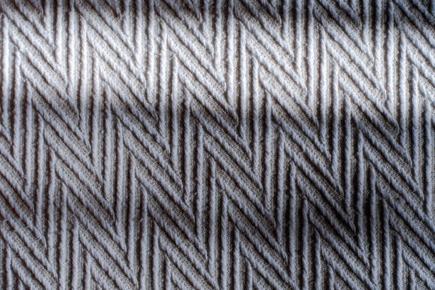 eine nahaufnahme der grauen tagesdecke von oben. die sonnenstrahlen beleuchten die textur und das gewebe des stoffes. zickzack- oder chevron-muster. - chevron textile striped close up stock-fotos und bilder